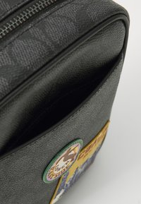 Schwarze strukturiertes Leder Tasche mit Reißverschluss, mit einem grünen und gelben Patch-Detail. Das Innere ist unliniert und hat eine offene Tasche.