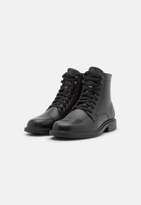 Botas de tobillo de cuero negro con cordones, con una textura suave, punta redonda, diseño minimalista y una suela baja y plana.