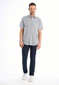 Camicetta a maniche corte con motivo floreale azzurro su sfondo bianco, abbinata a pantaloni blu navy e sneaker bianche. Look pulito e casual.