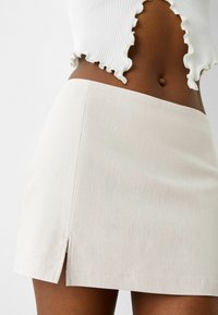 Witte geribbelde crop top met gerafelde randen, gecombineerd met een lichtbeige minirok met een zijsplit en een gladde textuur, minimale details.
