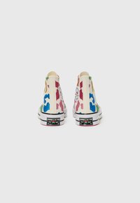 Høytopp kanvas sneakers i hvitt med flerfargede glitrende kamuflasjemønstre. Har svart gummisåle og Converse All Star-logo.