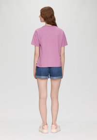 Rosa Baumwoll-T-Shirt mit kurzen Ärmeln, kombiniert mit Denim-Shorts mit umgeschlagenem Saum, vor einem neutralen Hintergrund.