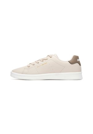 Zapatilla de piel sintética beige con suela blanca, punta redonda, diseño con cordones y acento contrastante oscuro en el talón. Detalles perforados minimalistas.