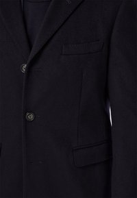 Námornícky blazer z vlnenej zmesi s hladkou textúrou, tromi prednými gombíkmi a jednou náprsnom vreckom. Obsahuje prispôsobené klopy a detaily šitia.