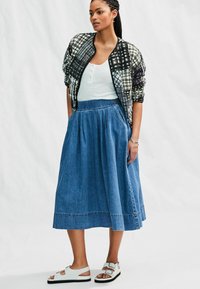 Jachetă bomber cu carouri alb-negru, top fără mâneci alb cu model în relief, fustă midi din denim albastru și sandale albe cu talpă neagră.
