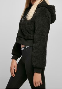 Czarna krótka bluza z kapturem wykonana z teksturowanej dzianiny polarowej, z kapturem, długimi rękawami i ściągaczami na mankietach, w zestawie z czarnymi legginsami.