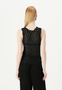 Svart blonde tank top med en figursydd design, med et teksturert mønster og uten ermer. Nederkanten er litt lengre bak.