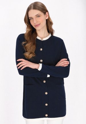 Námořnický modrý cardigan se zlatými knoflíky, bílým límcem a kapsami. Hladká tkanina, střední délka a dlouhé rukávy.