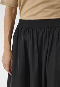 Fustă neagră, cu talie înaltă, dotată cu un brâu elastic pliat, realizată dintr-un material neted, cu o siluetă fluidă și fără modele vizibile.