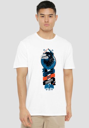 Young man wearing white t-shirt with a graphic of a black and blue raven and the words "Learning wit wisdom" in blue and orange.