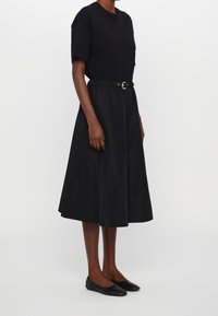 Svart T-shirt och ankellång kjol med skärp i midjan. Mjukt tyg med avslappnad passform, kombinerat med svarta platta skor.