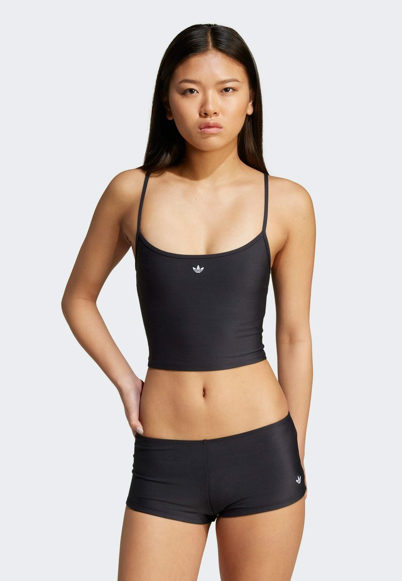 Top sportivo nero a maniche lunghe con spalline sottili e design aderente, abbinato a pantaloni corti neri a vita bassa con un piccolo logo.