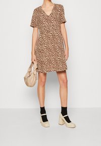 Hnědé šaty s krátkým rukávem a béžovým leopardím potiskem, s výstřihem do V a nařaseným pasem. Doplněné béžovou kabelkou a platformovými podpatky.