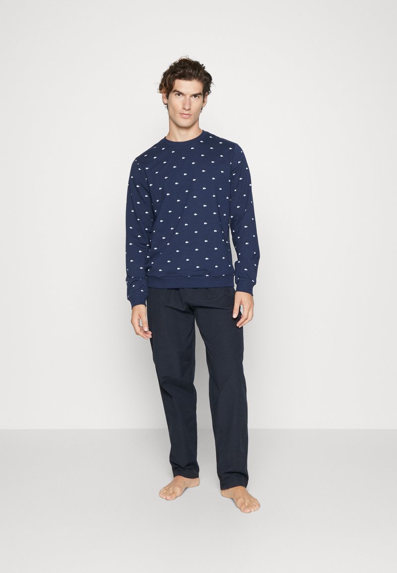 Langärmliger navy Pullover mit weißen Mustern, kombiniert mit dunklen Hosen. Der Stoff wirkt weich, hat einen Rundhalsausschnitt und gerippte Bündchen.