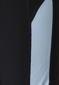 Czarne legginsy sportowe z jasnoniebieskim bocznym panelem. Wykonane z elastycznej tkaniny z widocznym przeszyciem wzdłuż szwów.