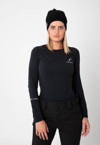 Black long-sleeve base layer with textured design, featuring a logo on the chest and sleeve, paired with black adjustable high-waisted pants and a knit beanie.