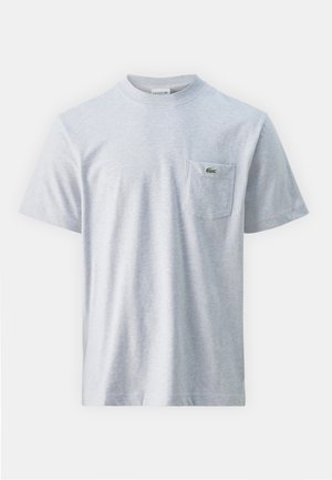 Camiseta de algodón gris con mangas cortas, escote redondo y un bolsillo en el pecho izquierdo que presenta un pequeño logo verde. Textura suave, corte casual.