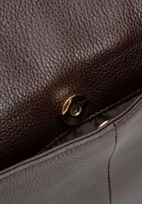 Interieur van een bruine leren handtas met een gestructureerde afwerking, gouden hardware drukknoopsluiting en een gladde voering met naaddetails.