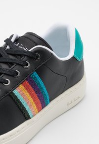 Svart lädersneaker med färgglada broderade ränder (turkos, lila, orange, teal) på sidan och en vit yttersula.