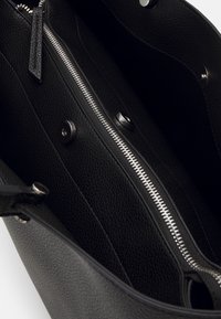 Svart läderväska inuti med texturerade väggar, silverdragkedja och metallknappstängningar. Har en rymlig design och minimal hårdvara.