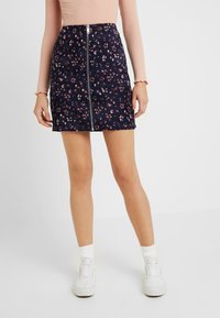 Marinblå kjol med blommönster och framzipper, tillverkad av strukturerad tyg. Kombinerad med vita sneakers och en randig rosa topp.