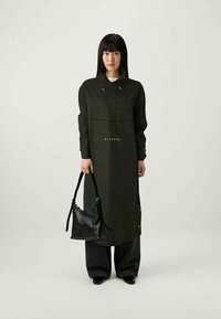 Μακριά ελιά-πράσινη φόρμα με κουκούλα, μπροστινές τσέπες και κορδόνια; συνδυασμένη με μαύρη τσάντα και σκούρα τζιν παντελόνια. Ορατή μινιμαλιστική επωνυμία.