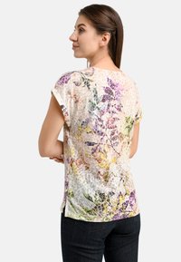 Kurze Bluse mit Blumenmuster in Creme, die eine Mischung aus lila, gelben und grünen Mustern zeigt, aus leichtem, strukturiertem Stoff.