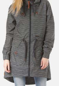 Cappotto a righe grigio scuro con cappuccio, caratterizzato da accenti marroni, cordini e ampie tasche frontali. Maniche lunghe e orlo posteriore più lungo.