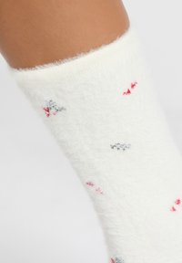 Biała, puszysta skarpetka o miękkiej fakturze, z rozproszonym wzorem małych czerwonych i szarych kwiatów. Z mankietem u góry.