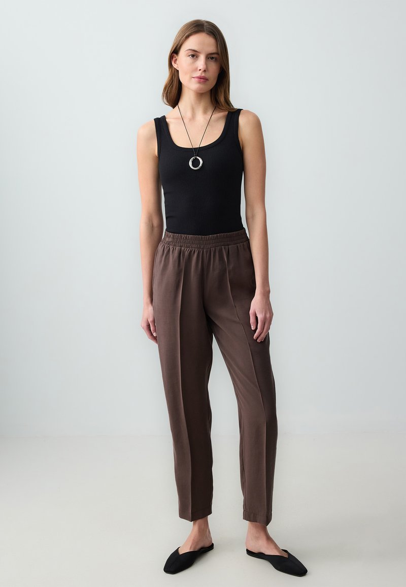 Débardeur noir à côtes, pantalon marron à taille élastique et chaussures noires à enfiler ; tissu lisse avec une coupe décontractée, sans motifs ni accents visibles.