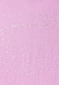 Tissu rose avec une surface texturée, présentant des points argentés brillants dispersés et la phrase "inspire-toi" en impression métallique.