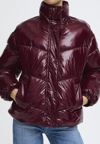 Bordeaux pufferjakke med en skinnende finish, høj krave, trykknapper, diagonale syninger og elastiske manchetter. Har frontlommer.