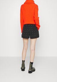 Suéter de punto rojo con cuello alto, combinado con pantalones cortos de mezclilla negros con tachuelas blancas. Botines verde oliva con suela gruesa.