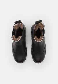 Botines negros de cuero con un suave forro de piel marrón, detalles decorativos de brogue en la puntera y lengüetas para facilitar su uso.