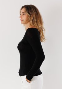 Top fitted nero a maniche lunghe con scollo rotondo, realizzato in un materiale liscio e elasticizzato; indossato con pantaloni bianchi, che mettono in risalto una silhouette slim.