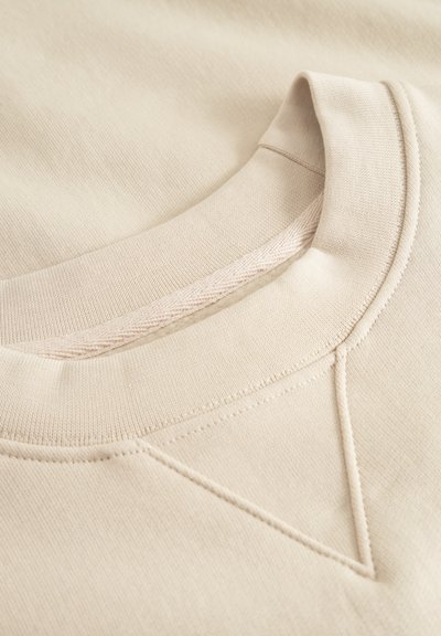 Beiger Pullover mit geripptem Rundhalsausschnitt. Verfügt über eine strukturierte Oberfläche und ein dekoratives Gesticktes Detail an der Schulter.