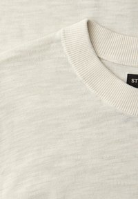 Gros plan sur un pull en maille de couleur crème montrant l'encolure ras du cou côtelée et le tissage texturé du tissu.