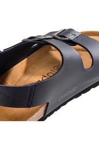 Sandalo in pelle nera con design aperto, dotato di una cintura con fibbia e di un fodero in sughero testurizzato. Cuciture a contrasto visibili. Suola in gomma.