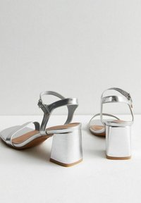 Silver höga klacksandaler med blockklack, med en slät metallisk yta, öppen tå-design och justerbar vristrem.