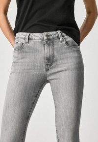 Grå denimjeans med en tettsittande design, som har en dragkedja i grenen, framfickor och ett subtilt tvättmönster på tyget.