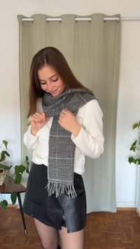 Szary i czarny szalik we wzór pepitki z frędzlami na końcach, noszony na białym swetrze, w połączeniu z czarną spódnicą. Wnętrze z roślinami.