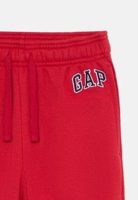 Røde joggebukser med elastisk liv med justerbare snorer og brodert "GAP"-logo i marineblå. Mykt, strukturert materiale.