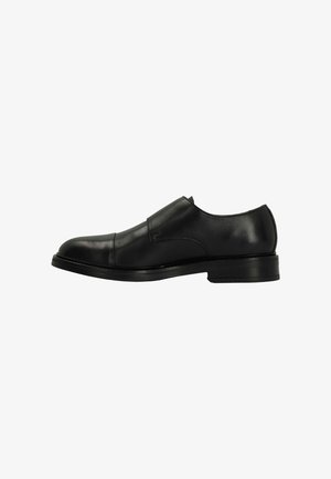 Black leather slip-on shoe featuring a rounded toe, smooth texture, minimalistic design, and a low stacked heel. No visible hardware or embellishments.
