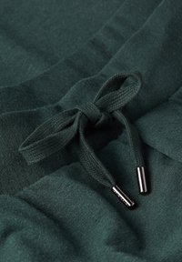 Groene stof met een gestructureerde afwerking heeft een koord met een strik, met metalen aglets aan de uiteinden. Eenvoudig, casual ontwerp.