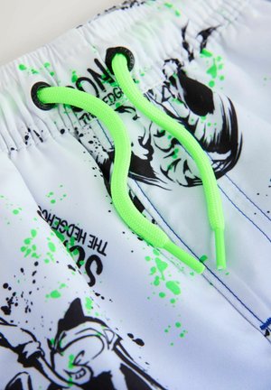 Baltas peldbikses ar melniem grafiskiem rakstiem un zaļa izšļakstījuma rakstiem. Tās ir aprīkotas ar zaļām aukliņām un elastīgu jostasvietu.