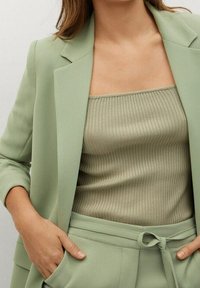 Blazer vert clair sur un haut beige à côtes. Le blazer présente un design structuré et des revers à encoches, tandis que le haut est ajusté et texturé.