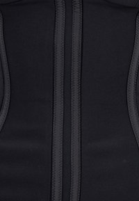 Tessuto in neoprene nero con due cuciture verticali, caratterizzato da bordi testurizzati e un interno liscio. Costruzione resistente per abbigliamento sportivo.