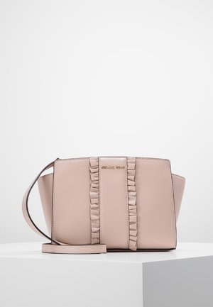 Hellrosa Michael Kors Umhängetasche mit Rüschen entlang der Mitte und einem dünnen verstellbaren Träger, auf einer weißen Oberfläche platziert.