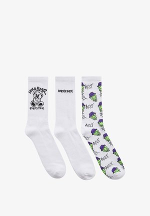 Tre paia di calze: bianche con orsetto grafico nero, bianche con "west coast" e calze colorate con facce verdi che indossano cappelli viola.