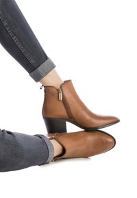 Bruine leren enkellaarsjes met een puntige neus, zijrits en een gestapeld hak, gecombineerd met opgerolde donkere jeans.